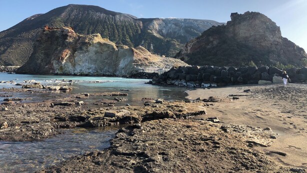 Una playa rocosa con una gran montaña al fondo.