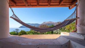 Una hamaca bajo techo de madera, con vista a un paisaje costero con montañas y el mar.