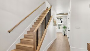 Een moderne trap met houten treden en zwarte leuningen, die leidt naar een goed verlichte gang met witte wanden en een houten vloer.