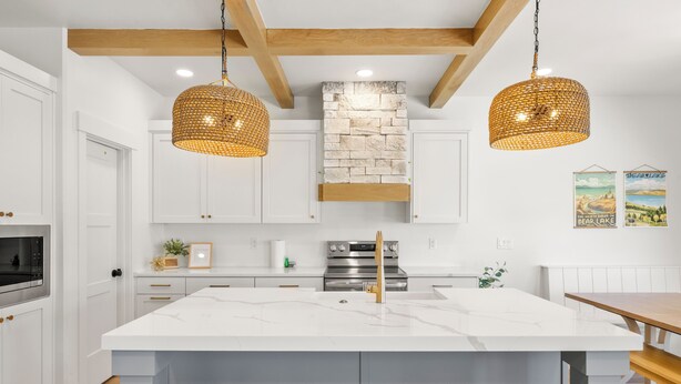 Een moderne keuken met witte kasten, een groot eiland met krukken, een accentmuur van steen en hangende rieten pendelverlichting.