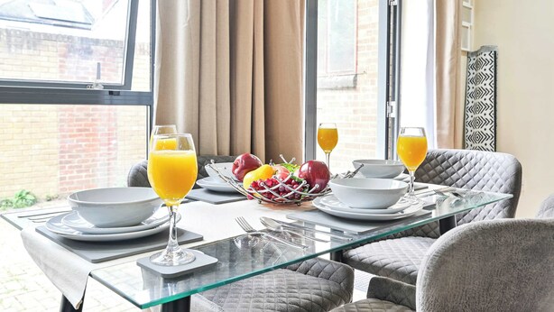 Une table de petit-déjeuner dressée avec des fruits, du jus d’orange et des assiettes blanches.
