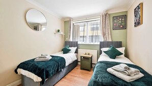 Une chambre avec deux lits, un miroir rond, une petite table de chevet et une fenêtre avec des rideaux.