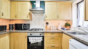 Une cuisine avec des meubles en bois, un four à micro-ondes, une cuisinière, un lave-vaisselle et une fenêtre avec des rideaux.