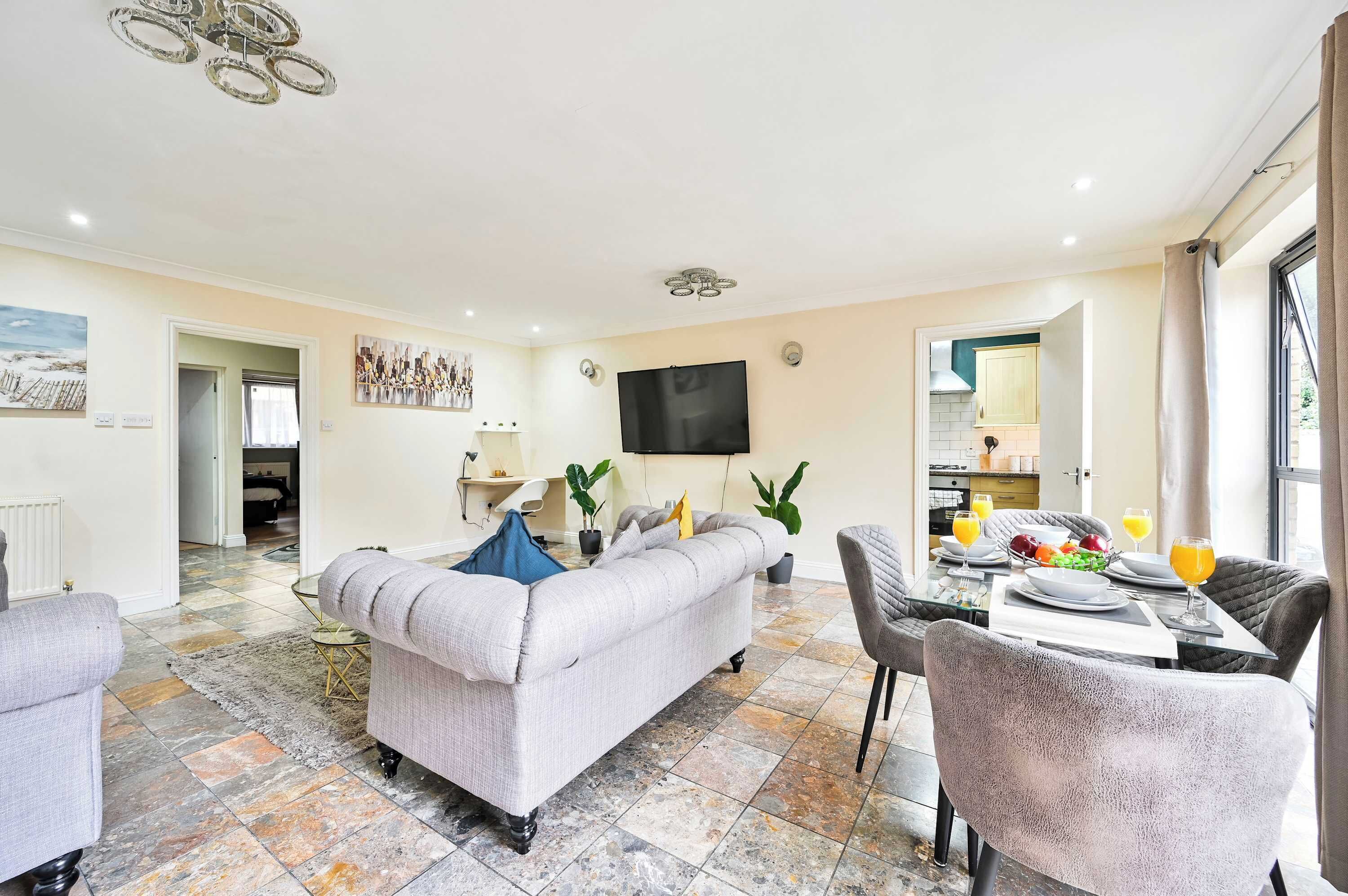 A living room with a sofa, dining table with chairs, a TV, and a kitchen in the background.