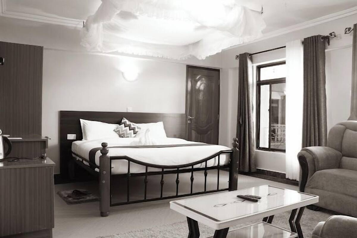 Una habitación de hotel con cama, mesita de noche y ventana con cortinas.