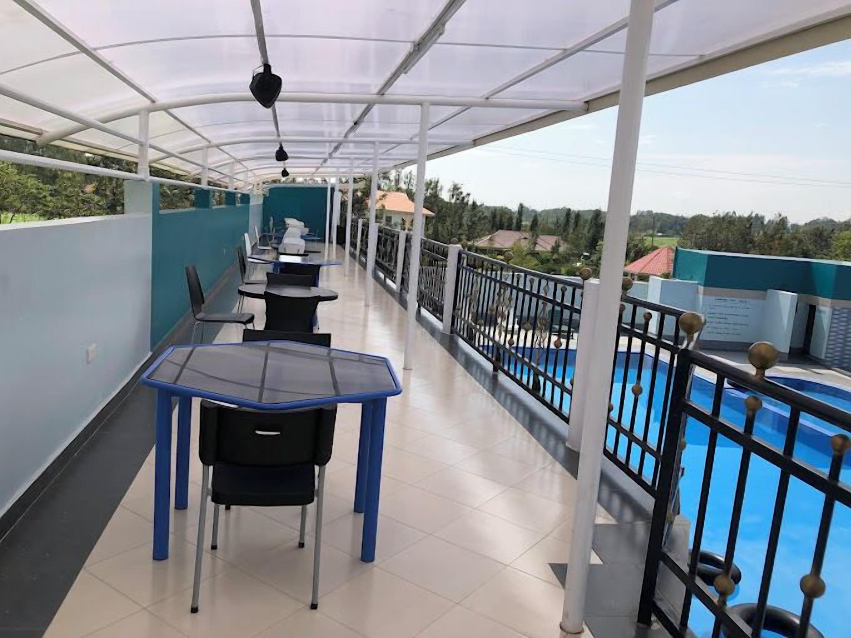 A covered outdoor area with tables and chairs, a pool, and a view of the surrounding landscape.