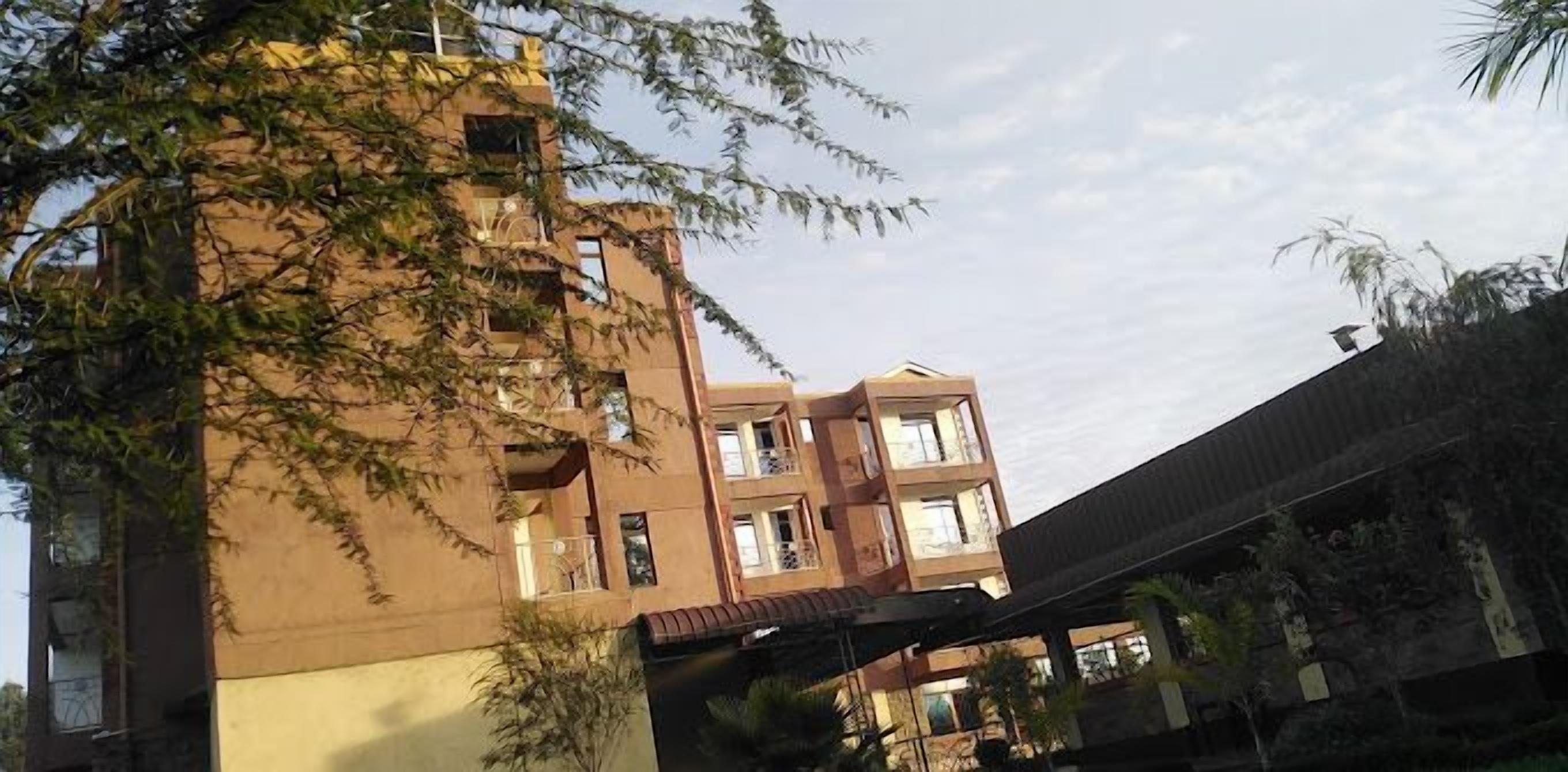 A multi-story building with balconies and windows, surrounded by trees.