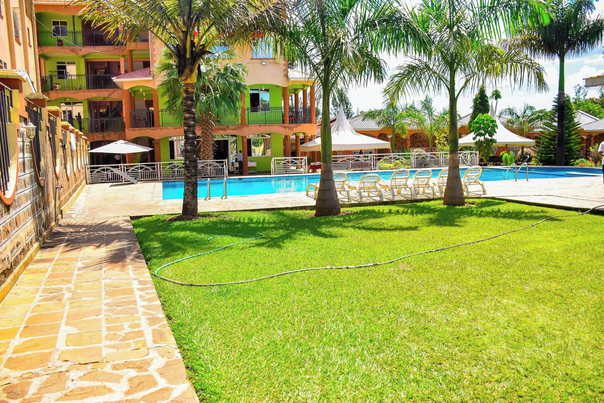 Un área de piscina con un sendero de piedra, palmeras y un edificio con balcones.
