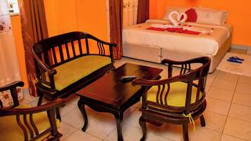 Habitación de hotel con una cama, dos sillas de madera con cojines, una mesita y un control remoto sobre la mesa.