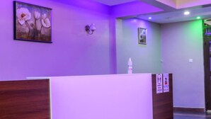 A reception area with a wooden reception desk, purple walls, and a painting of flowers.