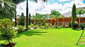 A well-maintained garden with a variety of tropical plants and a building with a tiled roof. - Hotel Vannah (Migori)