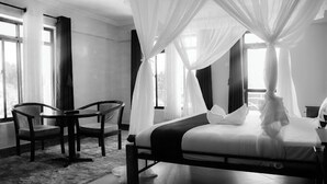 A bedroom with a bed under a canopy, a chair, and a small table. - Hotel Vannah (Migori)