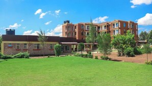 A multi-story building with a flat roof, surrounded by a well-maintained lawn and various trees. - Hotel Vannah (Migori)
