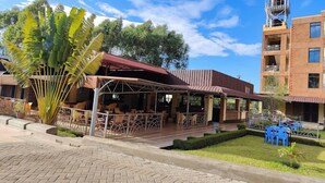 A covered outdoor seating area with tables and chairs, a water tank on a building, and a well-maintained lawn. - Hotel Vannah (Migori)