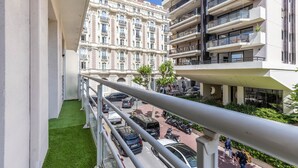 Ein Balkon mit Blick auf ein historisches Gebäude, ein modernes Gebäude und eine Straße mit Autos und Fußgängern.