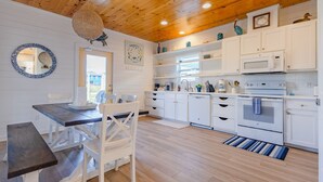 A modern kitchen with white cabinets, a wooden ceiling, and a dining area with a table and chairs.