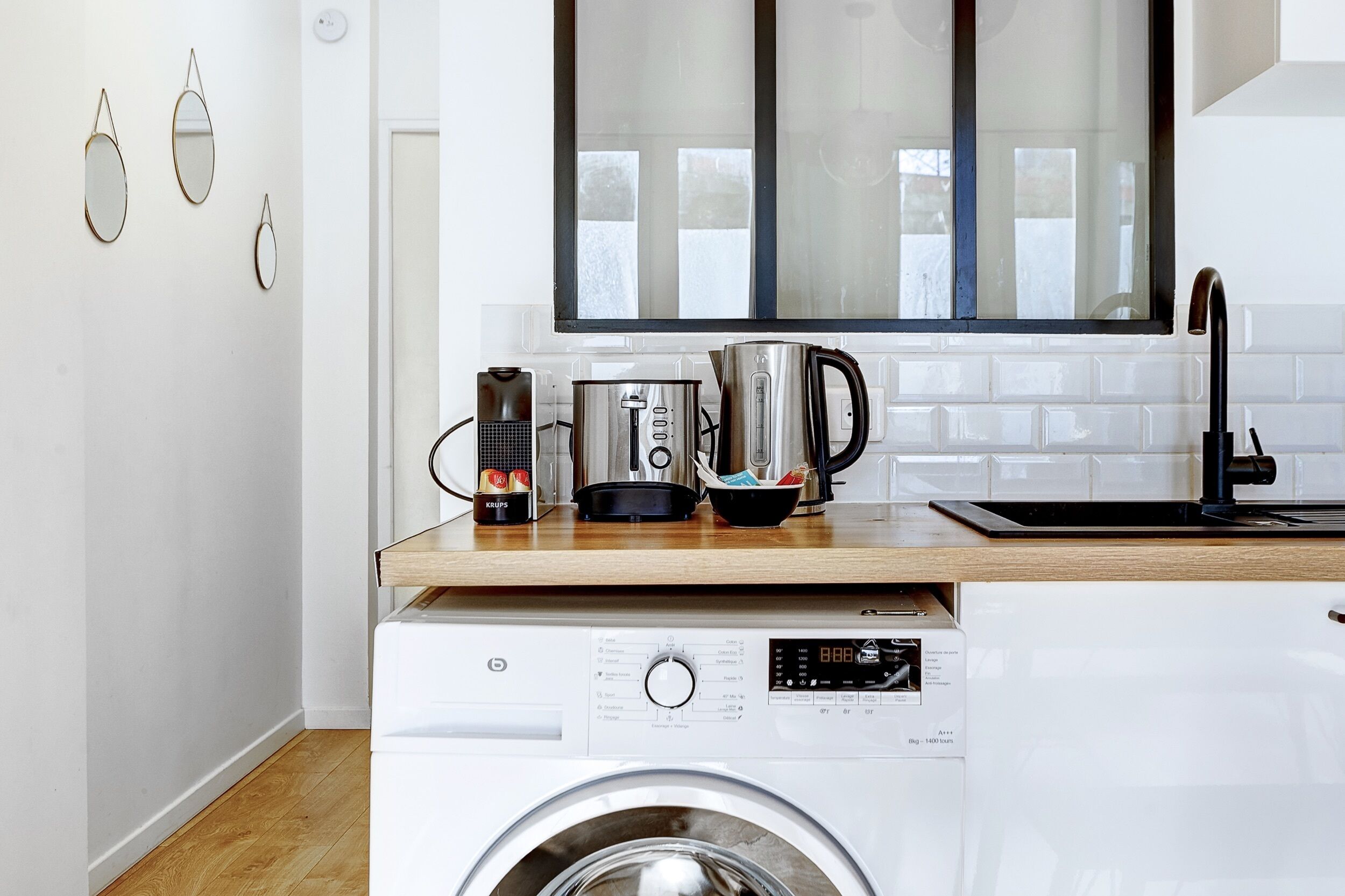 A compact kitchen with a washing machine, a kettle, and a coffee maker on the countertop.