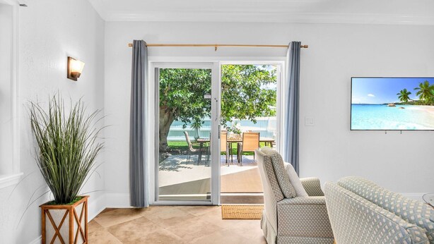 Ein Wohnzimmer mit einer Glasschiebetür, die auf eine Außenpatio mit Tisch und Stühlen führt.