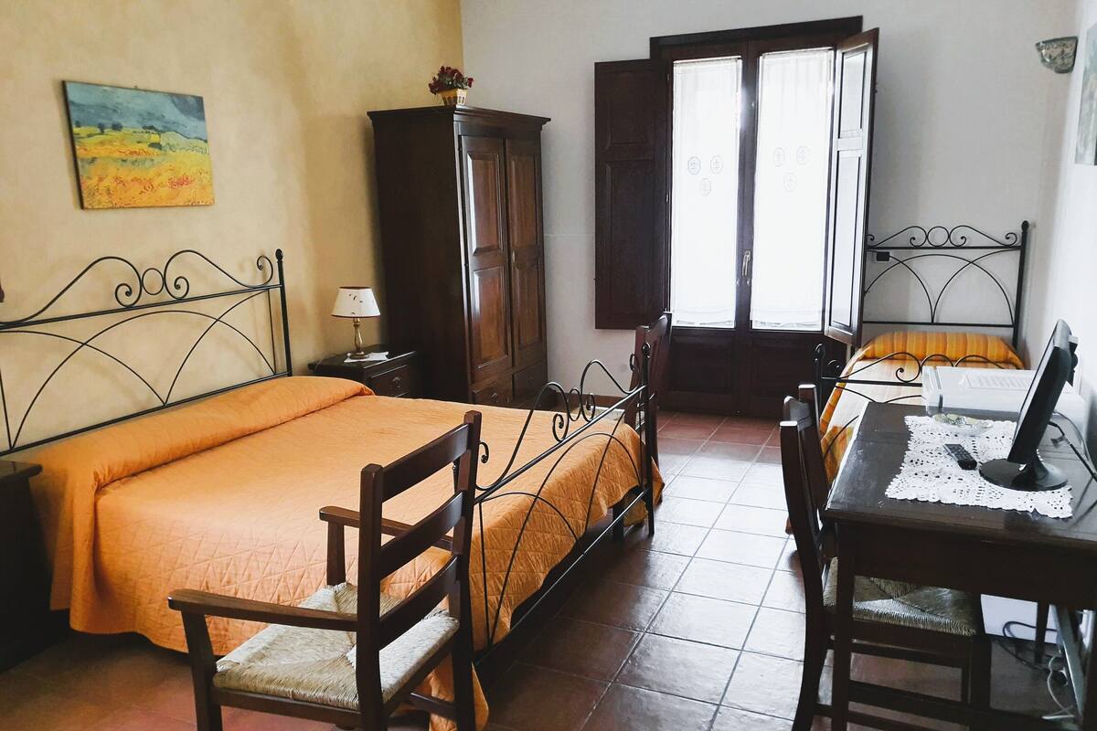 A bedroom with a bed, a desk with a computer, a chair, a wardrobe, and a window.