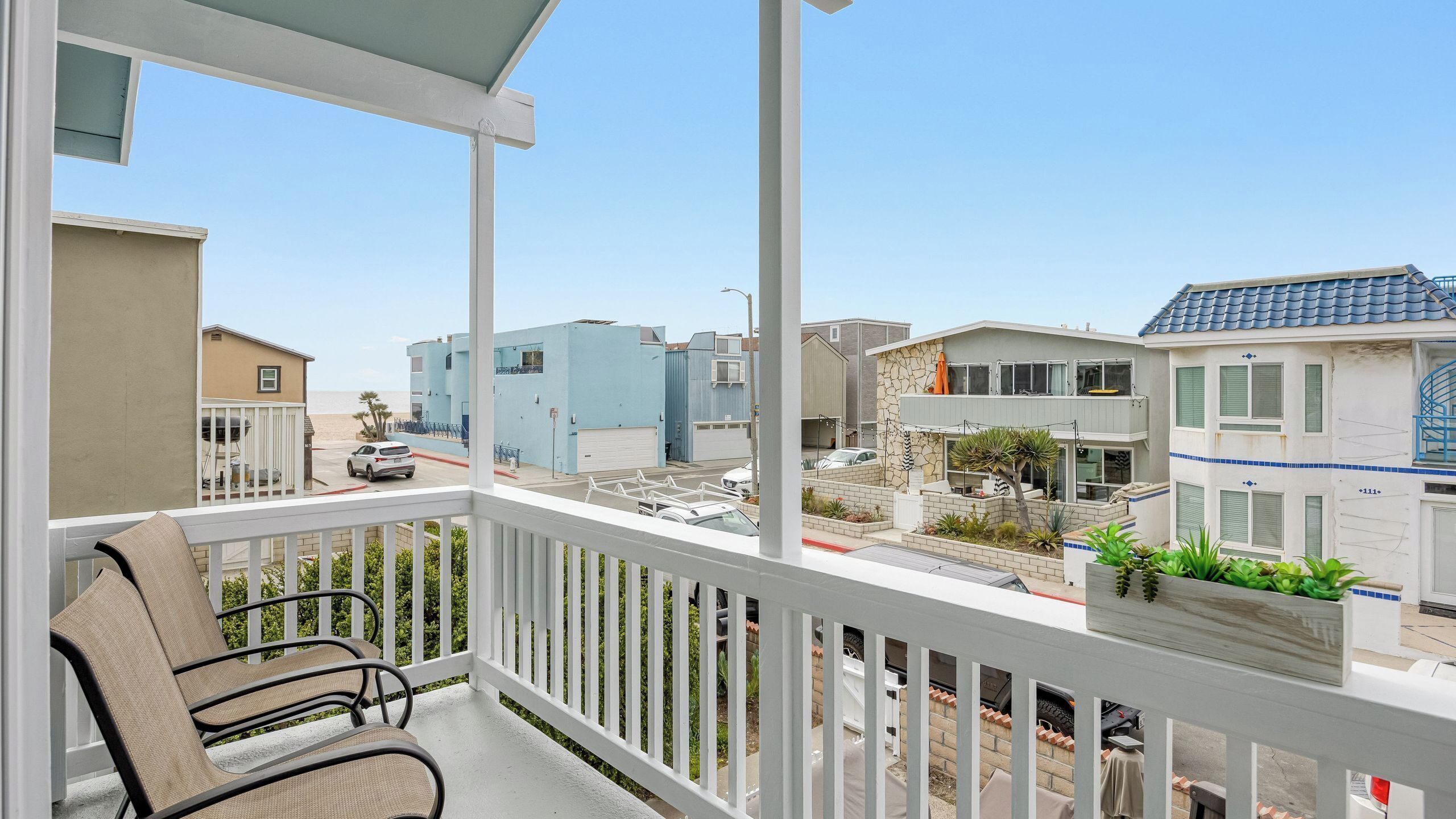 A balcony with outdoor furniture, a view of a residential area, and a clear sky.