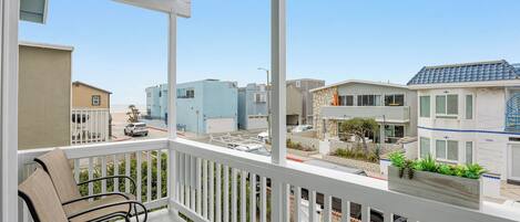 A balcony with outdoor furniture, a view of a residential area, and a clear sky.