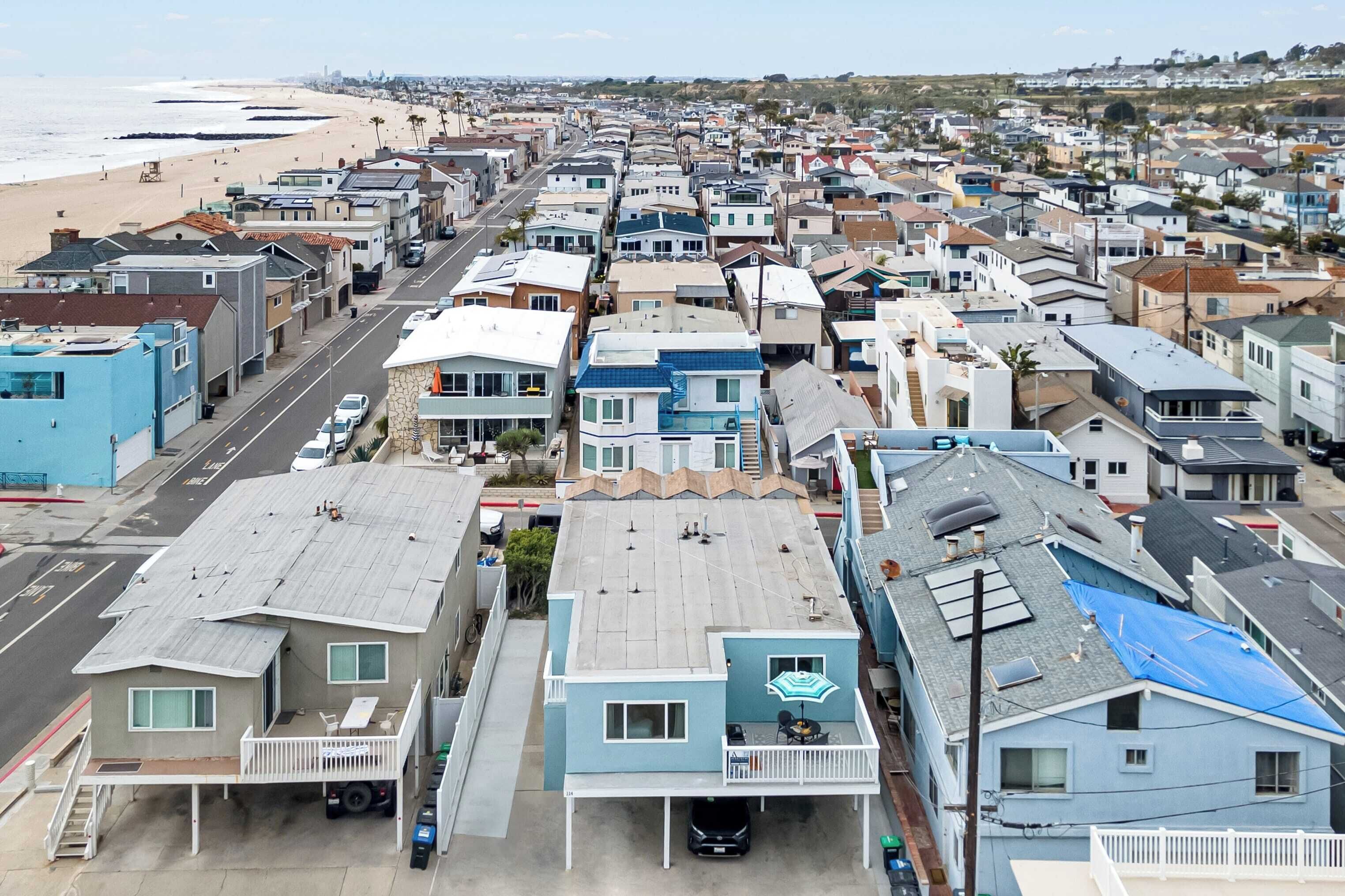 A coastal residential area with houses, a beach, and a clear sky.