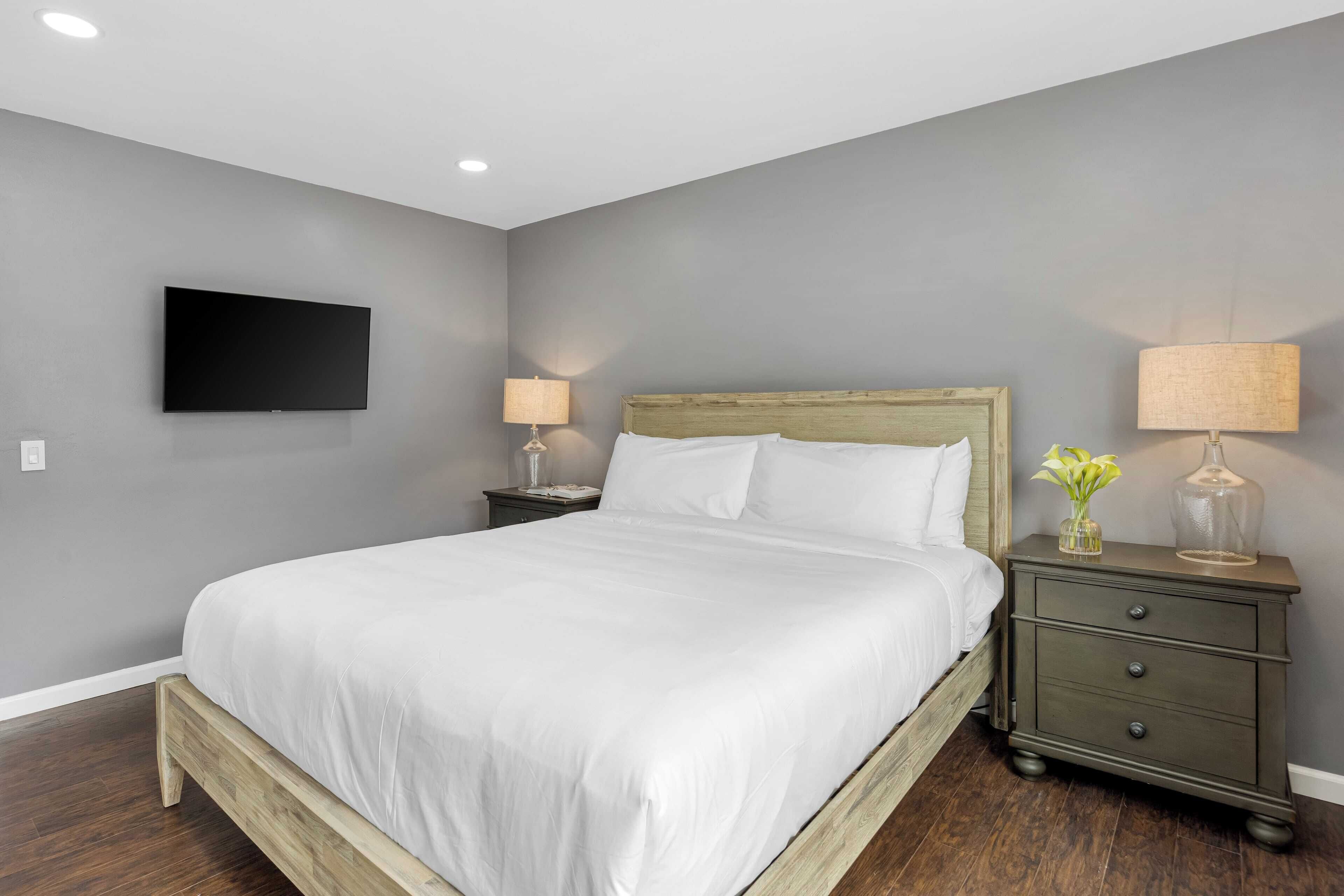 A bedroom with a bed, nightstands, a TV mounted on the wall, and a lamp on the nightstand.