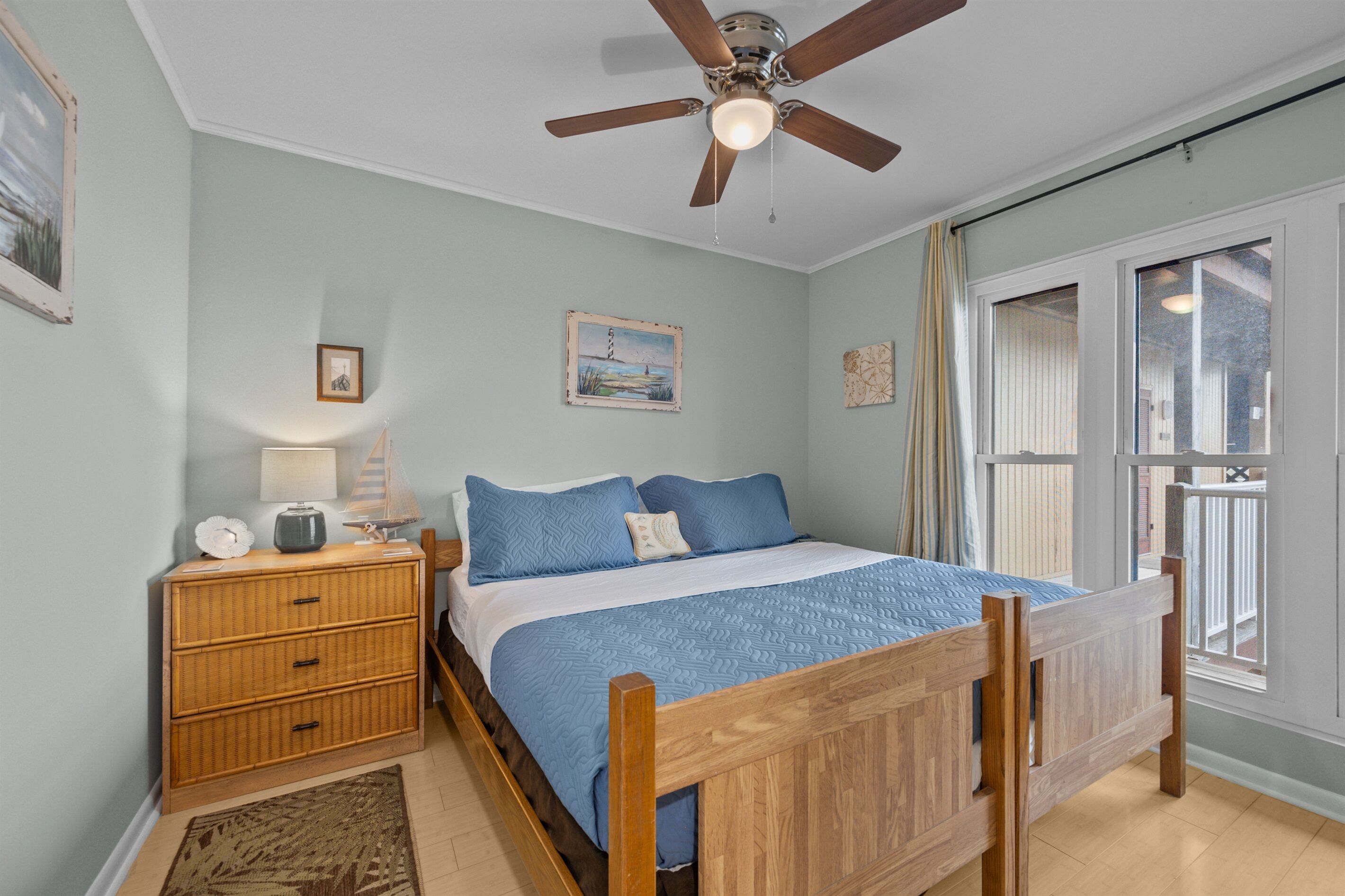 A bedroom with a wooden bed, a nightstand with a lamp, a ceiling fan, and a window with curtains.