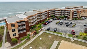 A multi-story hotel with a parking lot, a basketball court, and a view of the ocean.