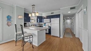 A modern kitchen with a central island, dark blue cabinets, white appliances, and a hanging light fixture.