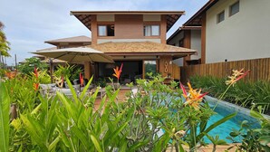 A two-story house with a swimming pool, surrounded by tropical plants and a wooden deck. - Casa Marluá (Camacari)