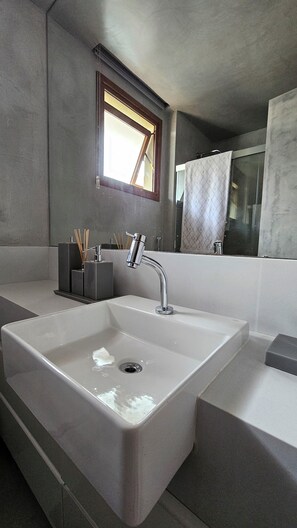A modern bathroom with a large rectangular sink, a chrome faucet, and a window with a wooden frame. - Casa Marluá (Camacari)