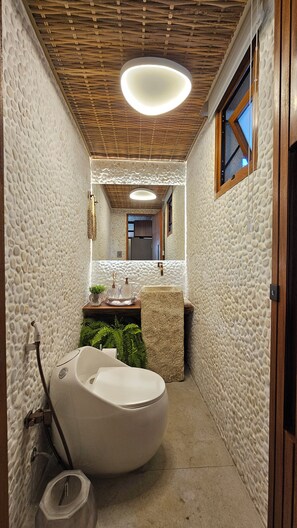 A narrow bathroom with a unique toilet design, a small sink, and a mirror. - Casa Marluá (Camacari)