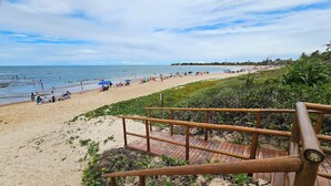 A beach with a wooden walkway leading to the shore, surrounded by greenery. - Casa Marluá (Camacari)