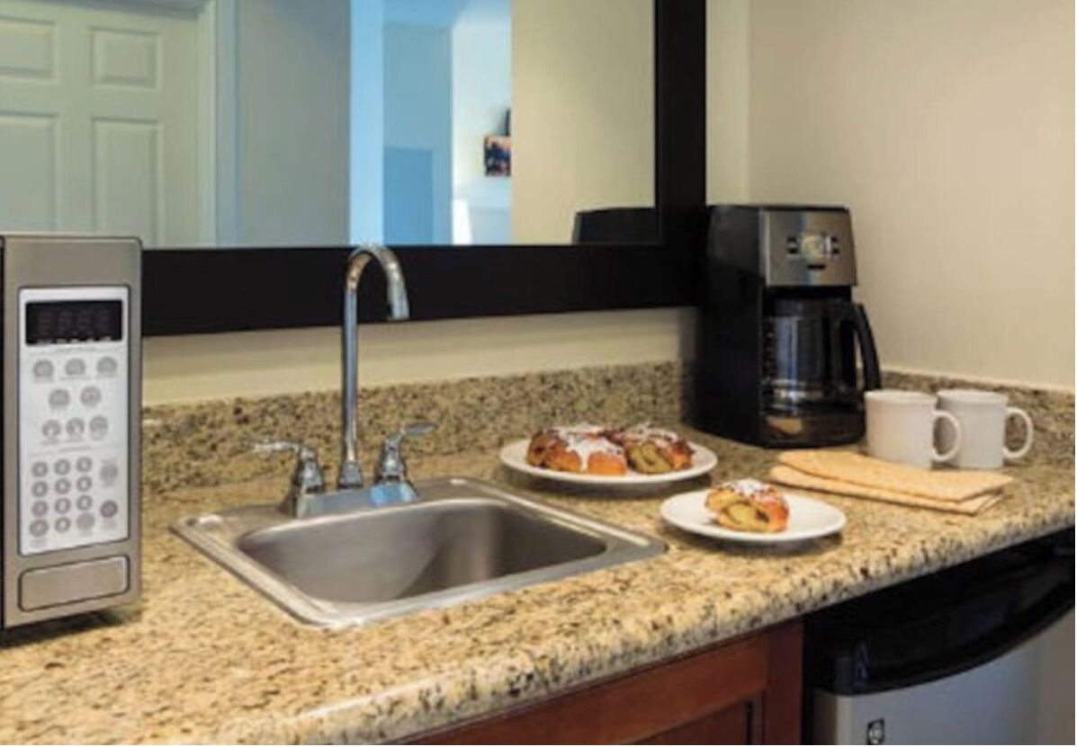 Cozinha com bancada de granito, pia de aço inoxidável, máquina de café e micro-ondas.