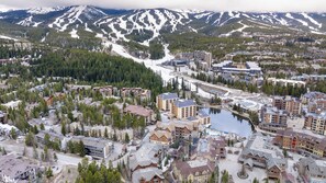 Un pueblo montañoso con una mezcla de edificios residenciales y comerciales, un cuerpo de agua central y picos nevados al fondo.