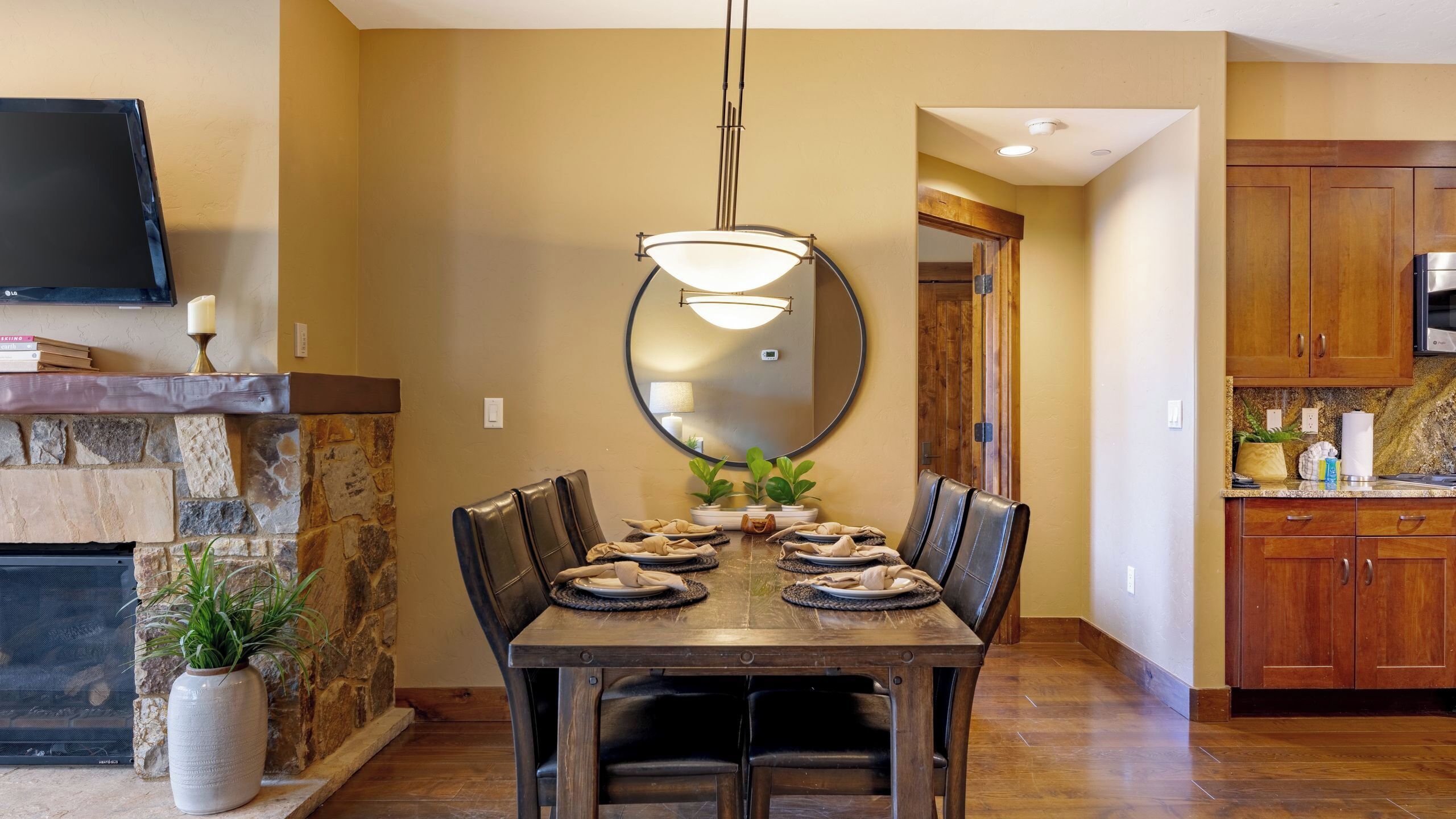 Un comedor con chimenea de piedra, un espejo grande y una cocina moderna con armarios de madera.