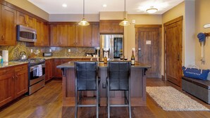 A kitchen with wooden cabinets, stainless steel appliances, and a central island with bar stools. - Steps to Lifts, Peak 9, Main Street Balcony, Lounge Pool Water House 5204 by Avantstay (Breckenridge)