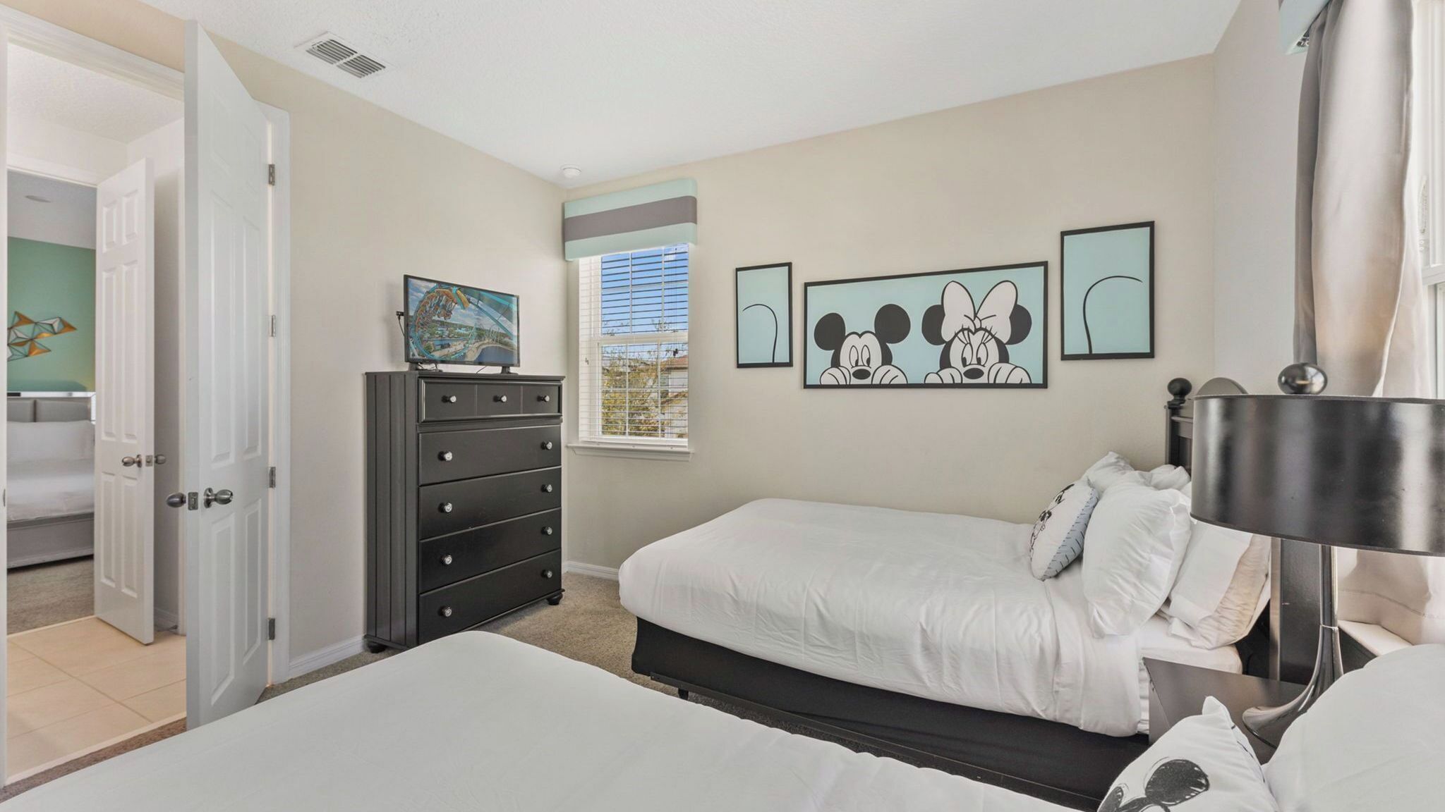 Une chambre à coucher comprenant un lit, une commode, une fenêtre avec des stores et des œuvres d’art murales.