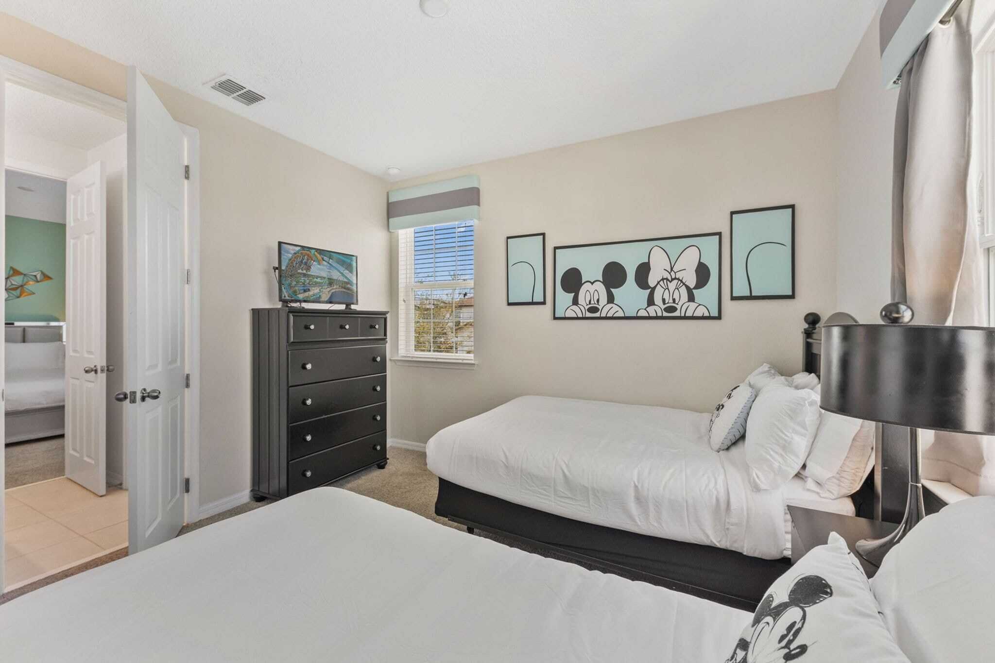 A bedroom with two beds, a dresser, and Mickey Mouse artwork on the wall.