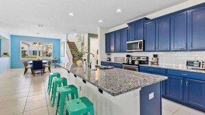 Een moderne keuken met blauwe kastjes, een granieten aanrechtblad en een centraal kookeiland met barkrukken.