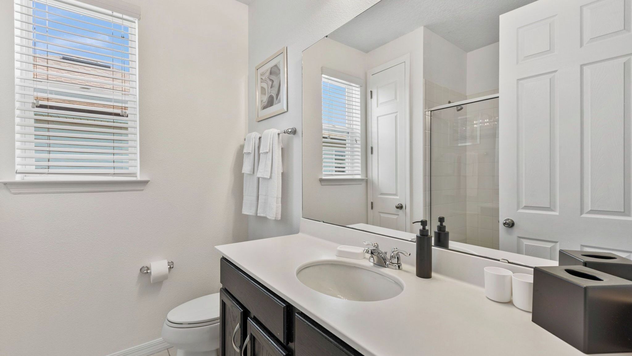 A bathroom with a white sink, a mirror, a toilet, and a window with blinds.