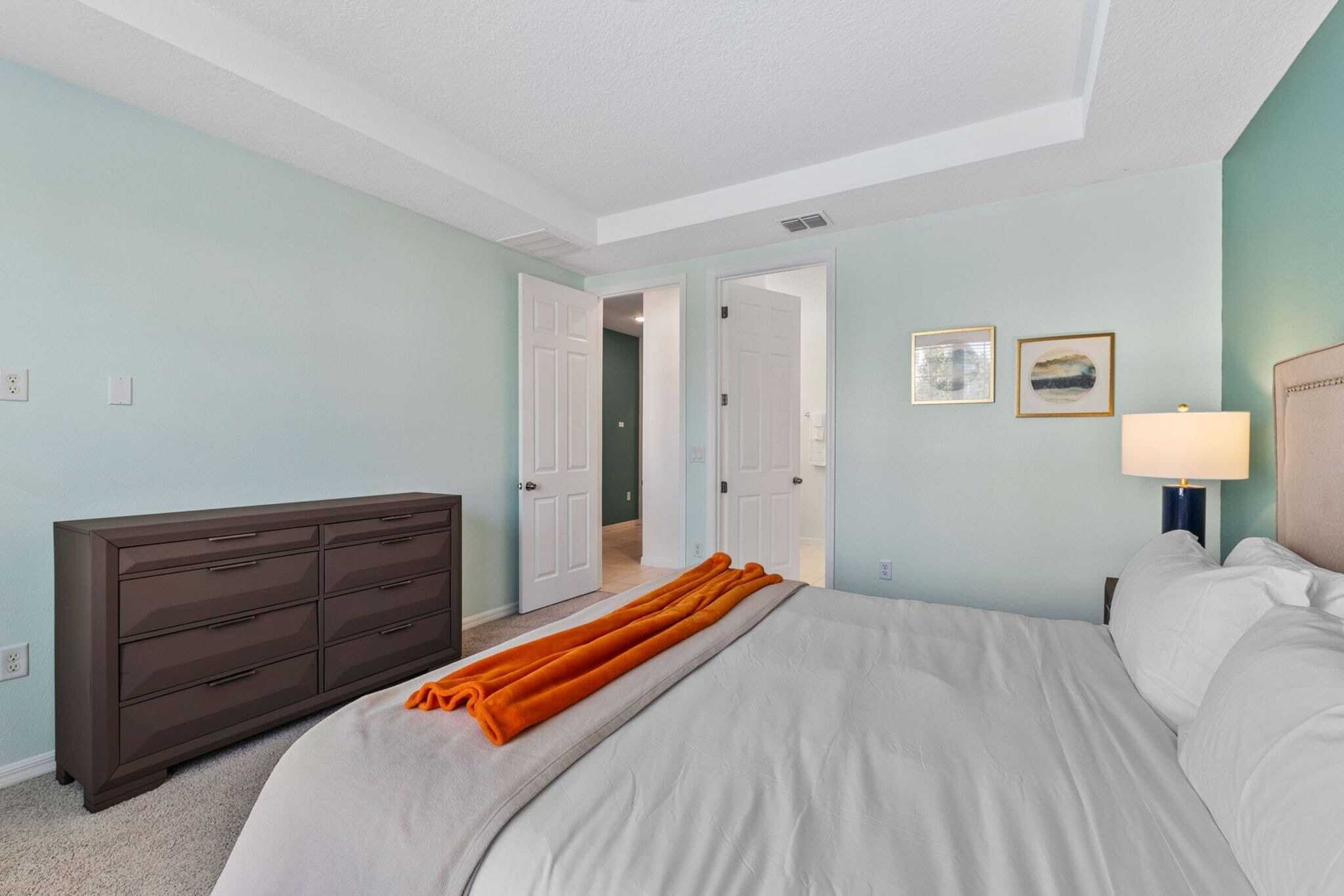 A bedroom with a bed, a dresser, and a door leading to another room.