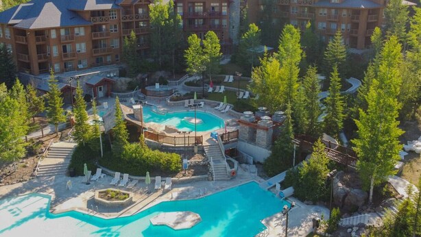 A resort with multiple buildings, a central pool area, and surrounding trees. - Creekside Lodge | Hot Tub | Ski-Out | Pool Table (Panorama)