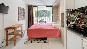 A compact room with a bed, a wooden table, a TV, and a balcony with a view.
