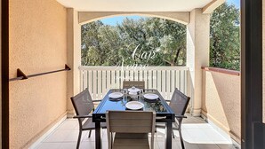 An outdoor patio with a table set for four, surrounded by chairs, and a view of trees through an arched window.