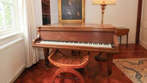 A grand piano in a room with a radiator, a wooden chair, a lamp, a framed portrait, and a patterned rug. - Higher Park Farm (Macclesfield)