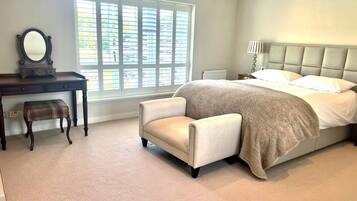 A bedroom with a bed, a desk with a mirror, a bench, and a window with blinds.