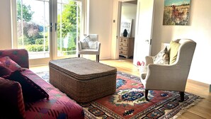 A living room with a large window, a wicker ottoman, a patterned rug, and a painting on the wall. - Higher Park Farm (Macclesfield)