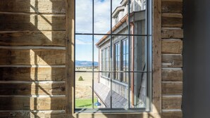 A log cabin interior with a large arched window, wooden walls, and a lantern on the floor. - Rustic Luxury Barn Retreat in Pray, Montana – Family & Pet Friendly (Livingston)